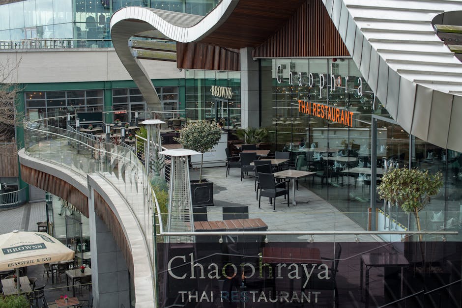 An outdoor terrace area of a restaurant at Brent Cross Shopping Centre, featuring several black dining chairs and square tables arranged for seating, with potted plants and modern outdoor heaters situ