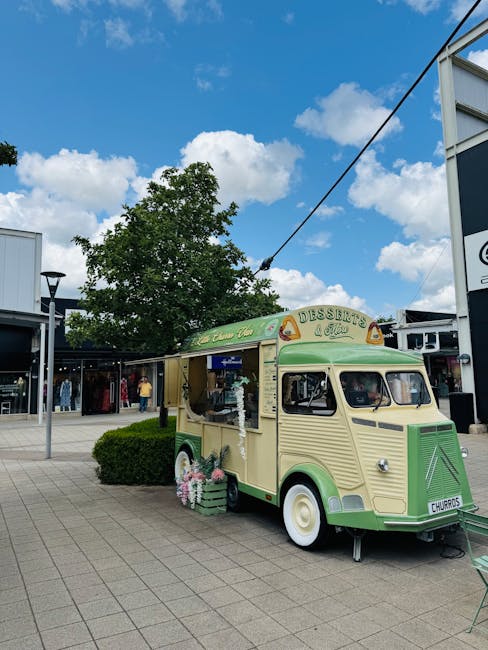 A vintage-style cream and green ice cream and dessert van, parked on a paved area outside a retail shopping centre in Brent Cross. The van is part of a moving or event setup, with a display window on 